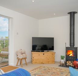 A living room with a wood stove television wooden chest and chair with blankets at Seamay in Polzeath