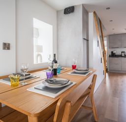 A dining table set with plates and glasses next to a kitchen with cabinets and appliances at Hoheck in Abersoch