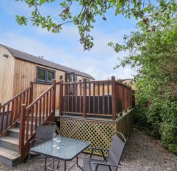 A small outdoor seating area with two chairs and a table next to wooden steps leading to a wooden cabin at The Retreat in Bangor-On-Dee