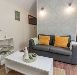 A living room with a gray sofa with yellow cushions a white coffee table and a small shelving unit at The Retreat in Bangor-On-Dee