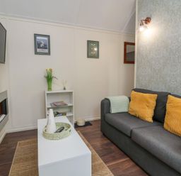 A living room with a gray sofa with yellow pillows a white coffee table a wall-mounted television and a fireplace at The Retreat in Bangor-On-Dee