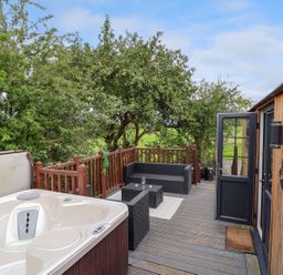 An outdoor deck with a hot tub seating area wooden railing and an open door at The Retreat in Bangor-On-Dee