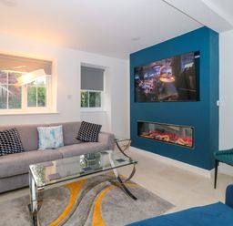 A living room with a grey sofa and cushions glass coffee table wall mounted tv and electric fireplace at 4 Noel Court in Chipping Campden