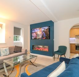 A living room with sofas a glass coffee table a mounted television and an electric fireplace at 4 Noel Court in Chipping Campden