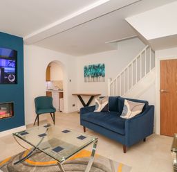 A living room with a blue sofa and chair glass coffee table and mounted TV above fireplace at 4 Noel Court in Chipping Campden