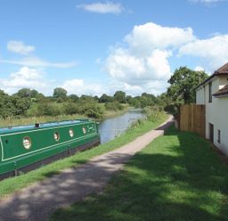 A canal boat moored next to a path by a river with a house on the right at Valley House in Halberton near Tiverton