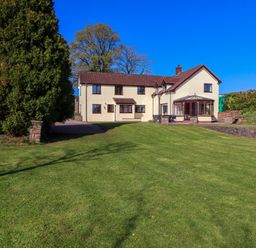 A two-story house with beige walls and brown roof with a large green lawn in front at Valley House in Halberton near Tiverton
