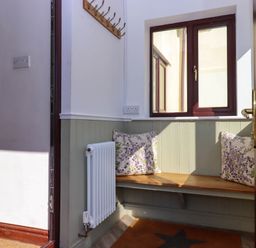 A small entryway with a wooden bench with floral cushions a radiator and a window at Valley House in Halberton near Tiverton
