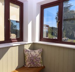 A corner window seat with floral cushions and brown window frames overlooking a garden at Valley House Halberton near Tiverton