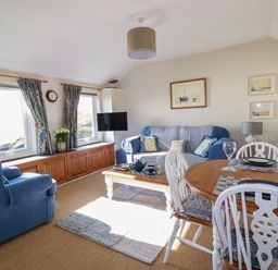 A living room with blue sofas a wooden dining table with white chairs and a mounted television at Suntrap House in Portloe