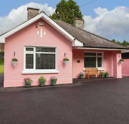 A house with a pink exterior and a bench outside at Rosemont in Adare