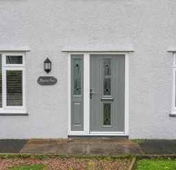 A front entrance with a gray door and two windows on a white textured wall at Monarfon Criccieth
