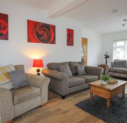 A living room with three sofas a coffee table a lamp and red rose paintings on the wall at Monarfon in Criccieth