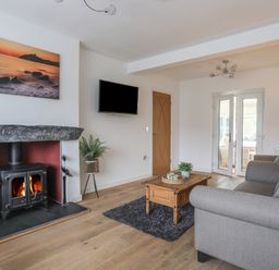 A living room with a wood burning stove a gray sofa a wooden coffee table and a wall mounted television at Monarfon in Criccieth