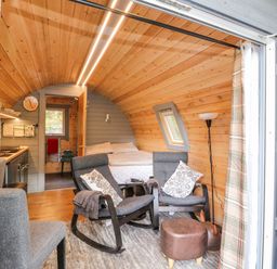 A small wooden pod interior with two gray rocking chairs, a bed, a kitchen area, and a floor lamp at Elleric Pods - The Last Resort Fasnacloich near Appin