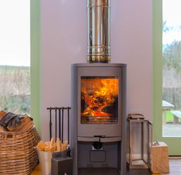 A wood burning stove with fire inside and firewood beside it in a room with glass doors at Smugglers Bodmin Moor St Breward near St Tudy