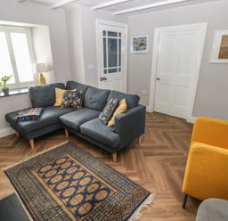 A living room with a gray sectional sofa and a yellow armchair and a patterned rug on a wood floor at Min-Y-Ffordd in Dinas Cross