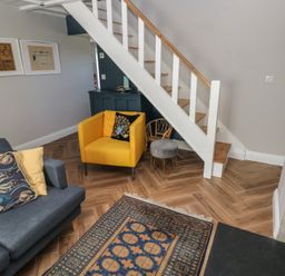A living room with a yellow chair blue sofa patterned rug and stairs at Min-Y-Ffordd in Dinas Cross
