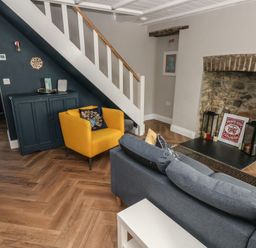 A living room with a yellow armchair a grey sofa a black cabinet under stairs and a stone fireplace at Min-Y-Ffordd in Dinas Cross
