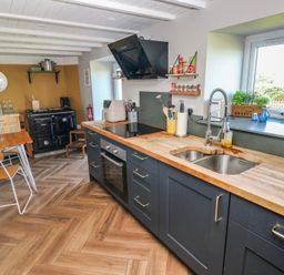 A kitchen with wooden countertops blue cabinets a double sink and a dining table with chairs at Min-Y-Ffordd in Dinas Cross
