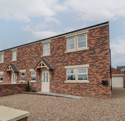 A brick exterior of a semi detached house with gravel driveway and small porch at Breamish Christon Bank near Embleton