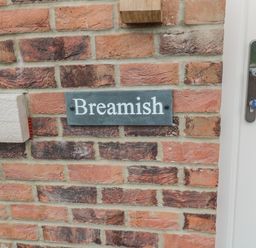 A brick wall with a nameplate reading Breamish next to a white door with a handle at Breamish in Christon Bank near Embleton