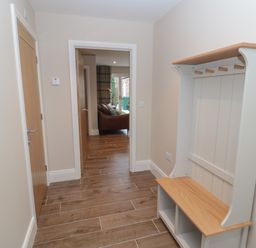 A hallway with wooden floor tiles a wooden door a coat rack with hooks and storage and a view into a living room at Breamish in Christon Bank near Embleton