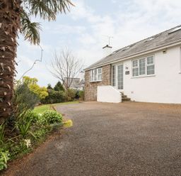 The exterior of a white house with stone detail and multiple windows with a driveway and plants including a palm tree at The Palms in Abersoch