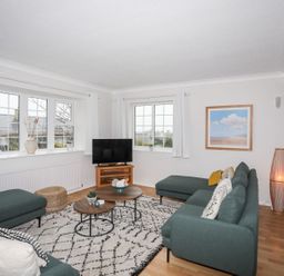 A living room with green sofas a TV on a wooden stand and framed beach painting at The Palms in Abersoch