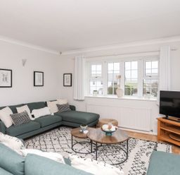 A living room with green sofas a wooden coffee table a patterned rug a TV on a wooden stand and framed pictures on the wall at The Palms in Abersoch