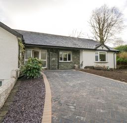 A driveway leading to a single-story house with a stone and white exterior at Whimhowe in Windermere