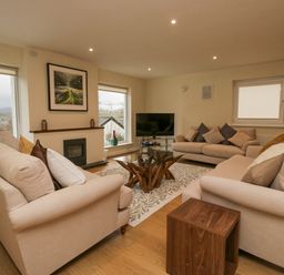 A living room with three beige sofas a glass coffee table a television and large windows at Whimhowe in Windermere