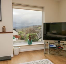 A living room with a large window showing an outdoor view and a television on a glass stand at Whimhowe in Windermere