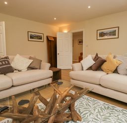 A living room with two beige sofas and a glass coffee table with wooden base at Whimhowe in Windermere