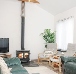 A living room with green leather sofas a wood burning stove and wooden chairs at The Dairy Barn in Camelford