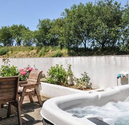 An outdoor area with a hot tub and wooden dining furniture at The Dairy Barn in Camelford