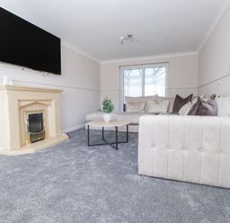 A living room with a beige fireplace a wall-mounted TV a light-colored sofa a round coffee table with a plant and glass doors at 9 Beckett Close in Colwyn Bay