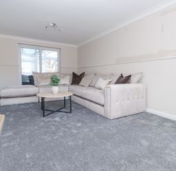 A living room with a beige sectional sofa a round wooden coffee table with a plant on it and a beige fireplace at 9 Beckett Close in Colwyn Bay