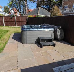 A backyard with a hot tub on a stone patio next to a grass lawn and wooden fence at 9 Beckett Close Colwyn Bay