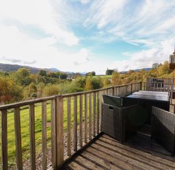 A wooden deck with black outdoor chairs and tables overlooking green fields and trees at Crathie Lodge Banavie near Caol