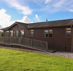 A wooden single-story house with a wheelchair ramp on a grassy lawn at Crathie Lodge in Banavie near Caol