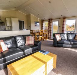 A living room with two black leather sofas a wooden coffee table and a dining table with chairs at Crathie Lodge in Banavie near Caol