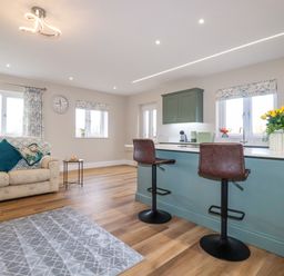 A kitchen with green cabinets and an island with two brown bar stools next to a living area with a beige sofa and a small table at Little Hillside in Redruth
