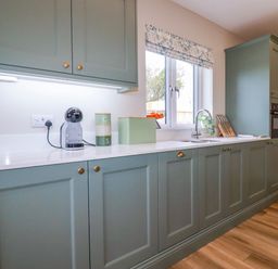 A kitchen with green cabinets a coffee machine containers a sink and a window at Little Hillside in Redruth