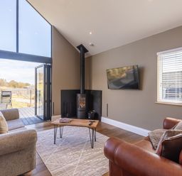 A living room with a grey sofa a brown leather sofa a wood stove and a TV on the wall at Hares Hill in Thornton-Le-Dale
