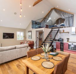 An open plan living room and kitchen with a wooden dining table and chairs a staircase leading to a loft bedroom at Hares Hill in Thornton Le Dale