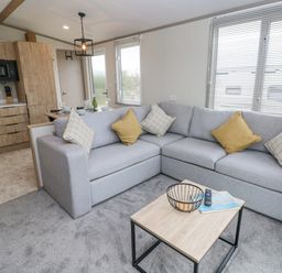 A living room with a grey sectional sofa and a wooden coffee table next to a kitchen with wooden cabinets at Caldey Retreat Hasguard Cross near Broad Haven