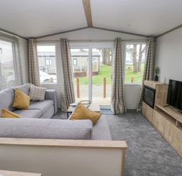 A living room with two gray sofas cushions a wooden coffee table a wooden TV unit with a TV and an electric fireplace and windows with checked curtains at Caldey Retreat Hasguard Cross near Broad Haven