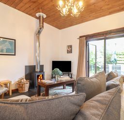 A living room with a fireplace a TV wooden coffee table gray sofa and sliding glass door at Owl Cottage in Ashen Cross Pelynt