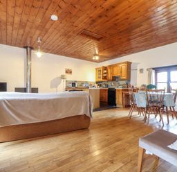 An open plan living area with a sofa a dining table wooden chairs kitchen cabinets and wooden ceiling at Court Cottage in Ashen Cross Pelynt
